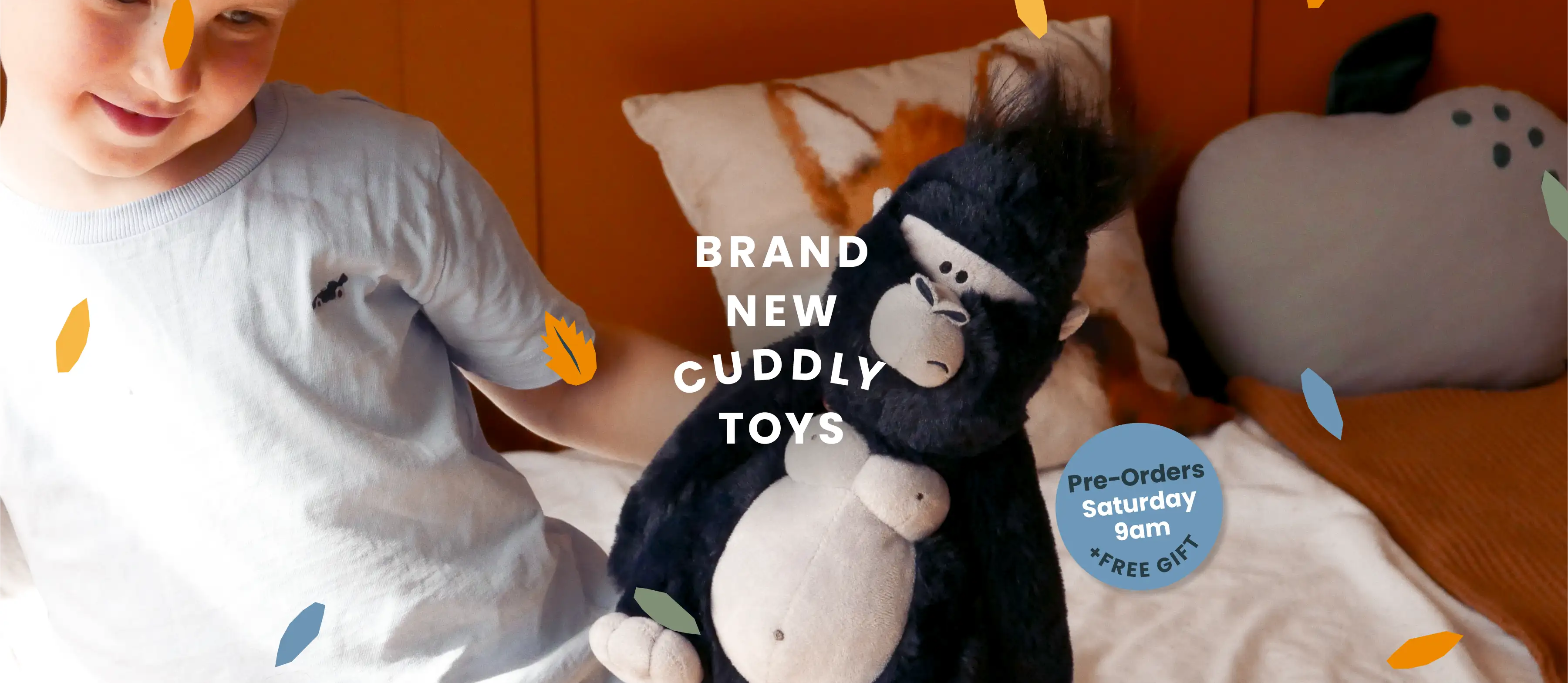 A child in a white t-shirt sits on a bed next to a black plush gorilla toy, with a gray plush character and pillows in the background. Text overlays read 'BRAND NEW CUDDLY TOYS' and 'Free Orders Saturday 5pm - FREE GIFT', with decorative falling leaf graphics.